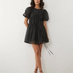 robes asymétriques à pois noir courte manches bouffantes crépon exclusivité portée par une femme avec des chaussures à talons noirs