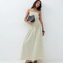 robes à pois jaune froncée la taille longue portée par un mannequin avec un sac noir et des sandales