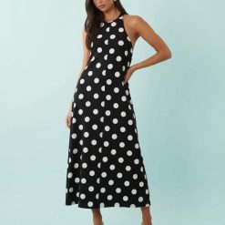 robes portefeuille à pois noir et blanc trapèze midi design sans manches col halter portée par une mannequin avec des mules noires