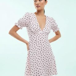 robes rétro à pois roses courte petite tissée imprimés femme asiatique portant robe rose à pois noirs col en v coupe évasée manches courtes plissées vindt un fond bleu ciel simple
