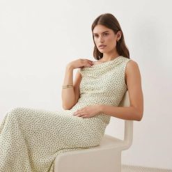 robes asymétriques à pois crème avec tombante épaule mollet longueur portée par une femme assise sur une chaise blanche