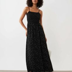 robes noires à pois blancs en tulle sans manches mi-longue portée par un mannequin sur un fond bleu avec un col rond et un ourlet à volant