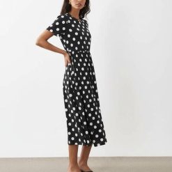 robes noires à pois blancs courtes jersey mi-longue manches courtes col rond fluide portée par un mannequin avec des talons noirs