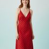 nuisettes à pois robe col v mi longue et rouge portée par une femme rousse avec des bretelles fines et des motifs noirs sur un fond bleu clair
