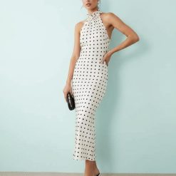 nuisettes à pois crème robe satin encolure licou détails fleurs longue ajustée portée par une femme avec pochette et talons noirs