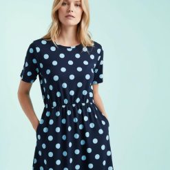 robes noires à pois blancs jersey mi-longue manches en bleu marine portée par une femme aux cheveux blonds sur un fond bleu clair