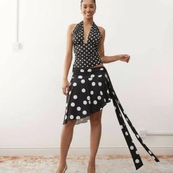 jupes courtes à pois noirs ensemble top décolleté plongeant asymétrique porté par un mannequin souriant avec des chaussures blanches