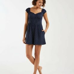 robes noires à pois blancs jersey mi-longue manches en bleu marine portée par une femme aux cheveux blonds sur un fond bleu clair