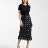 jupes courtes à pois satin dentelle bordée motif noir petite portée par un mannequin avec un haut noir et des escarpins noirs sur fond blanc