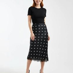 jupes courtes à pois satin dentelle bordée motif noir petite portée par un mannequin avec un haut noir et des escarpins noirs sur fond blanc
