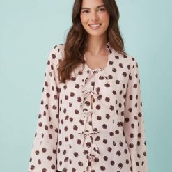blouses à pois roses encolure dégagée avec nœud portée par une femme souriante aux cheveux bruns avec des manches longues