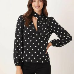 blouses à pois noirs et blancs avec détail foulard col en v manches longues portée par une femme