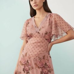 robes vintages rouges à pois manches évasées fleurie mi-longue dentelle multicolore rose portée par un mannequin sur un fond bleu clair avec col v et motifs de fleurs