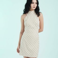 robes à pois jaune dos nu courte crème noirs portée par une jeune femme sur fond bleu pastel