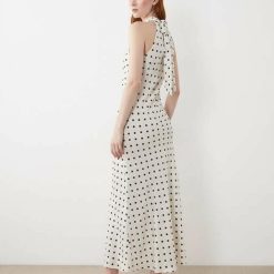 nuisettes à pois crème robe satin encolure licou détails fleurs portée par une femme vue de profil avec des talons noirs sur fond blanc