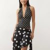 jupes courtes à pois noirs ensemble top décolleté plongeant asymétrique porté par une femme sur un fond blanc