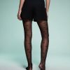 collants à pois noirs transparents femme motif fantaisie style portés de dos avec un short noir élégant sur un fond vert pastel clair