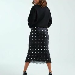 jupes courtes à pois satin dentelle bordée motif noir petite portee par un mannequin vue de dos avec des talons hauts noirs