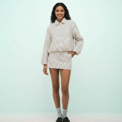 vestes à pois crème noirs boutonnée ensemble tissu technique col cordon serrage porté par une femme avec une jupe assortie sur fond vert clair