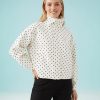 vestes à pois crème col courte et montant portée par une femme aux cheveux blonds avec un pantalon noir sur fond bleu clair