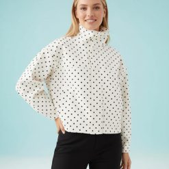 vestes à pois crème col courte et montant portée par une femme aux cheveux blonds avec un pantalon noir sur fond bleu clair