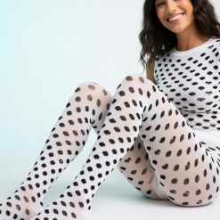 collants à pois motif cœurs rayés et noir portés par une femme souriante assise sur un fond blanc avec un haut assorti