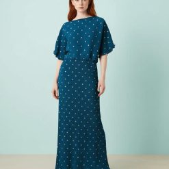 robes asymétriques à pois bleu sarcelle dénudées plissée longue métallisé épaules portée par un mannequin aux cheveux roux avec des sandales dorées