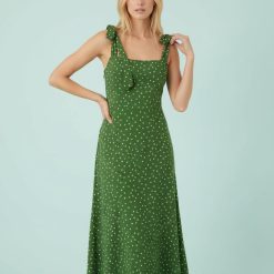 robes vertes à pois adrian bretelles nouées mi longue portée par une femme blonde sur un fond vert pastel clair