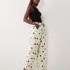 jeans à pois crème bouffant design pantalon coupe large imprimé avec des motifs ronds noirs porté par une femme avec un débardeur noir