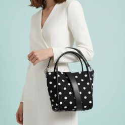 sacs de voyage à pois monochrome seau réglable avec bandoulière noir et blanc porté au bras par une femme habillée en blanc
