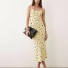 robes à pois jaune longue dos ouvert décolleté cœur caraco portée par un mannequin élégant tenant une pochette noire