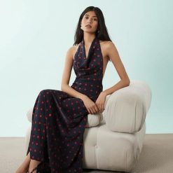 robes à pois marine bénitier col dos nu longue carmin portée par une femme assise sur un fauteuil beige élégant et élégamment posée