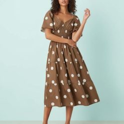 robes longues marron à pois blancs longueur mollet col v volants étagés portée par un mannequin avec des manches courtes et une taille smockée