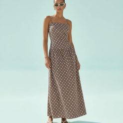 robes longues marron à pois chocolat bretelles fines lin découpe côté portée par un mannequin avec des lunettes de soleil et des sandales blanches sur un fond bleu clair