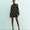 robes manches longues à pois courte ornementés noir doré portée par un mannequin avec col montant et motifs ronds dorés et noirs