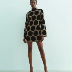 robes manches longues à pois courte ornementés noir doré portée par un mannequin avec col montant et motifs ronds dorés et noirs