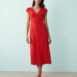 robes longues à pois rouge fluide col v avec mancherons portée par une femme élégante avec des sandales beiges sur un fond bleu