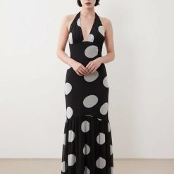 robes longues noires à pois corset style cintrée taille sirène ourlet evase avec decollete halter plongeant et motif a grands pois gris portee par un mannequin sur fond blanc