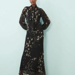 robes manches longues à pois nœud lavallière imprimé abstrait longue fluide noire et beige portée par un mannequin sur fond bleu clair