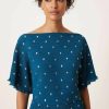 robes asymétriques à pois bleu sarcelle dénudées plissée longue métallisé épaules portée par un mannequin avec un col bateau et de petites fleurs dorées