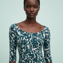 colliers à petit pois breloques poissons multi rangs doré porté par une femme vetue de une robe imprimee a motifs abstraits vert et blanc