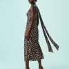robes asymétriques à pois satin longueur mollet foulard encolure marron portée par un mannequin avec des talons marron sur fond bleu clair