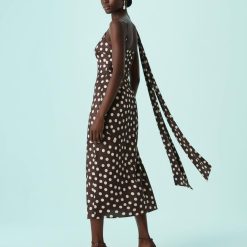 robes asymétriques à pois satin longueur mollet foulard encolure marron portée par un mannequin avec des talons marron sur fond bleu clair