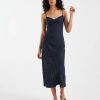 robes à pois marine buste torsadé nuisette mi-longue bleu portée par une femme aux cheveux bouclés avec des sandales noires sur fond blanc