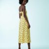 robes à pois jaune longue dos ouvert décolleté cœur caraco portée par une femme vue de dos avec des talons noirs sur un fond bleu clair