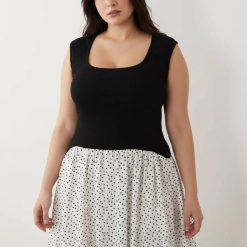 robes asymétriques à pois sans manches longue encolure dégagée monochrome élégante et moderne pour femme posant devant un fond clair