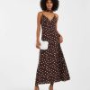 robes évasées à pois longue avec col foulard blanc chocolat portée par une femme avec pochette blanche et talons noirs