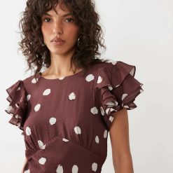 robes longues marron à pois évasées manches échancré dos portée par une femme aux cheveux bouclés avec des volants aux épaules et un motif à gros pois blancs