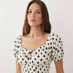robes à pois blanc et noir longue plage manches bouffantes liens devant une jeune femme portant une robe à pois blancs et noirs avec des manches bouffantes et un lien devant sur fond blanc