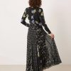 robes longues noires à pois imprimé fleuri col nageur avec manches ourlet godets vue de dos portée par un mannequin aux cheveux bouclés avec des talons noirs